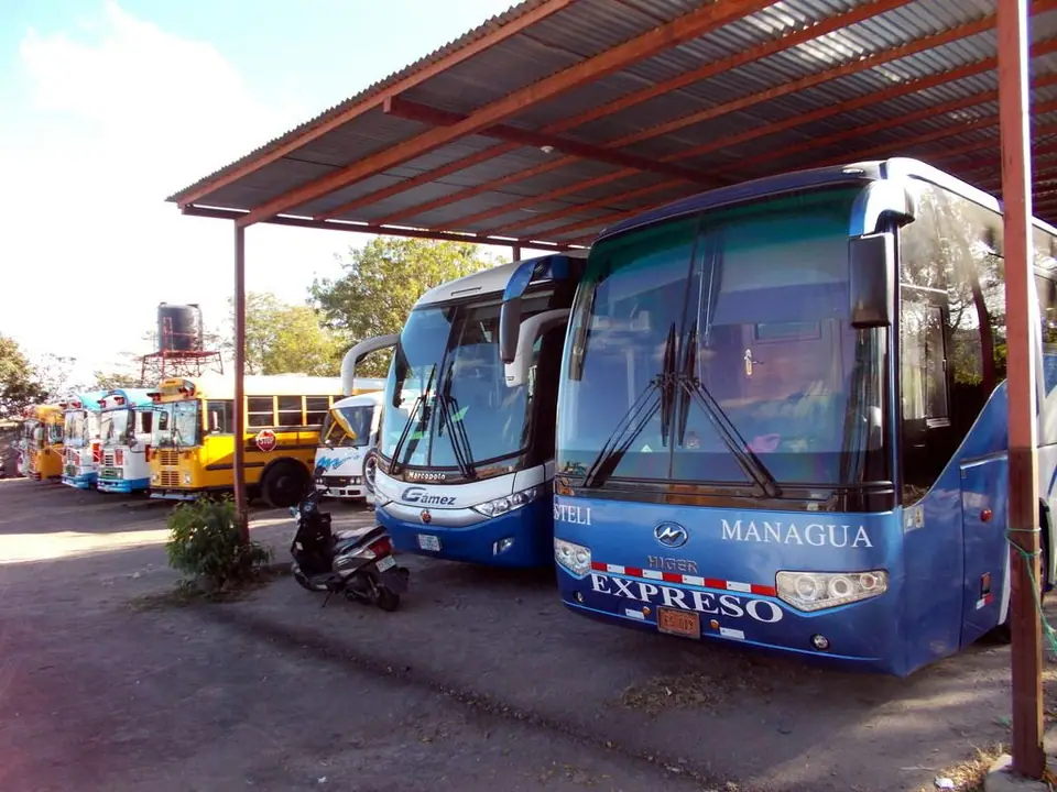Buses expresos azules con el rótulo «Managua Expreso» bajo un techo de zinc